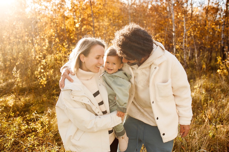 Smiling baby cuddled between parents in golden autumn light