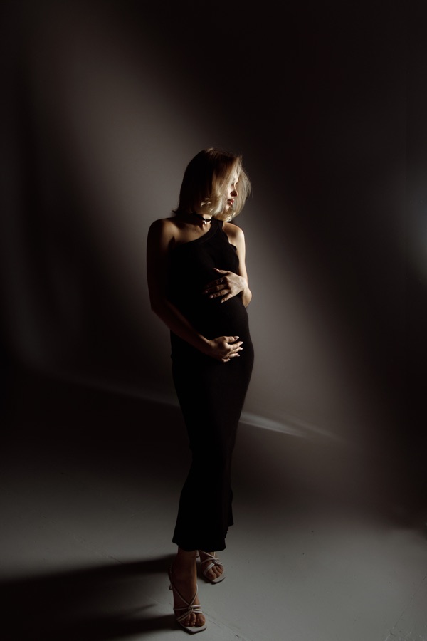 Maternity portrait in a black dress shaped by soft studio light