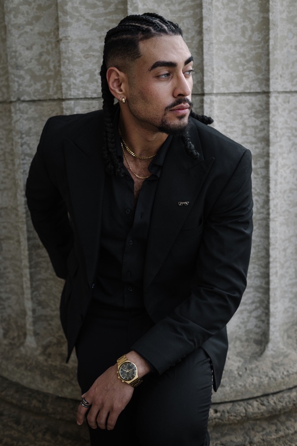 Editorial portrait of Karim in a black suit beside a stone column