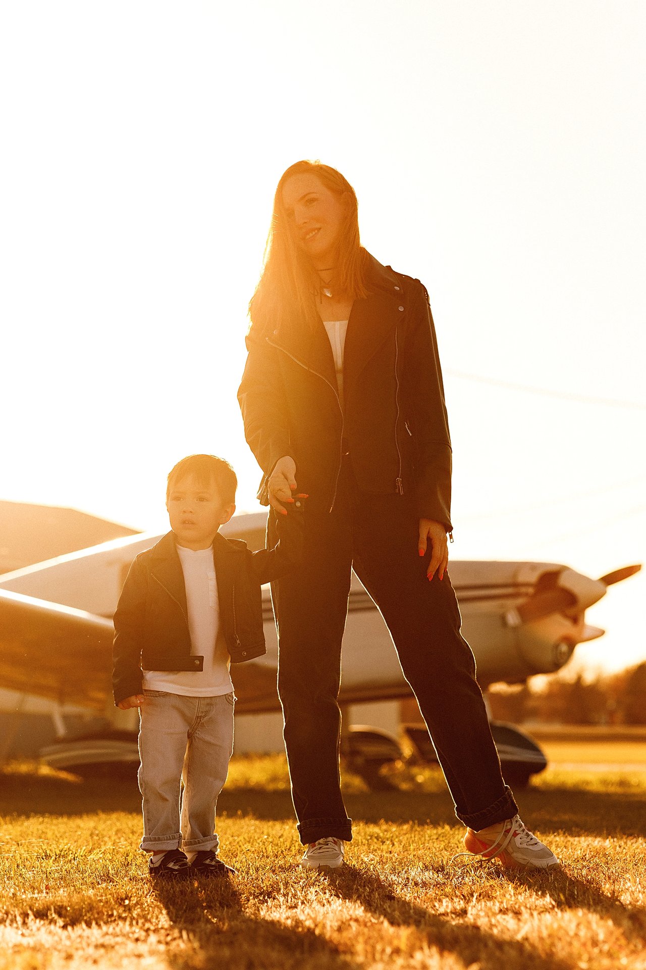 Alina and David holding hands on the grass in golden evening light with an aircraft behind them.