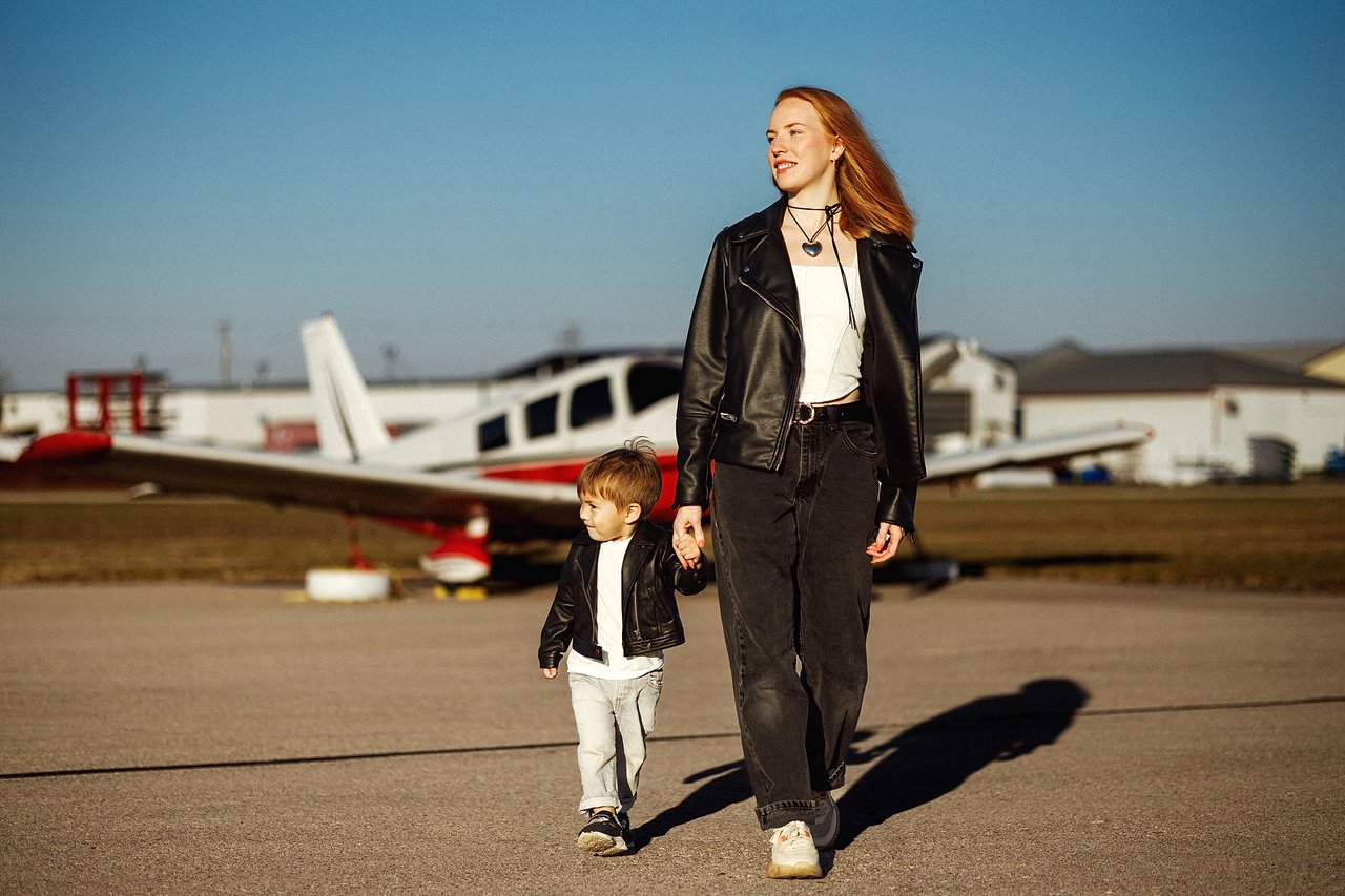 Alina and David holding hands as they walk past a small aircraft at the airport.