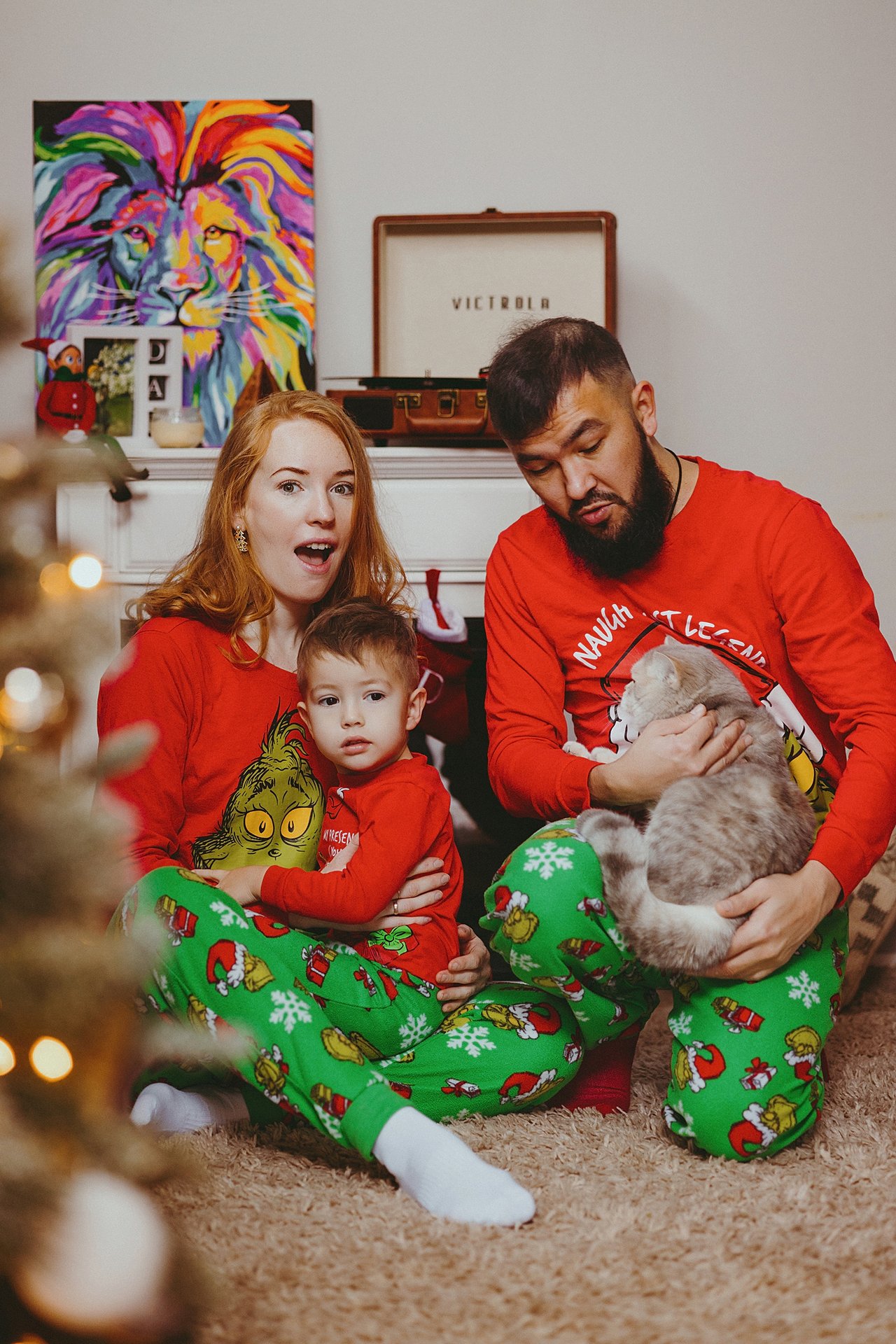 Alina and Nurali with their son David and cat, wearing matching Christmas clothes at home.