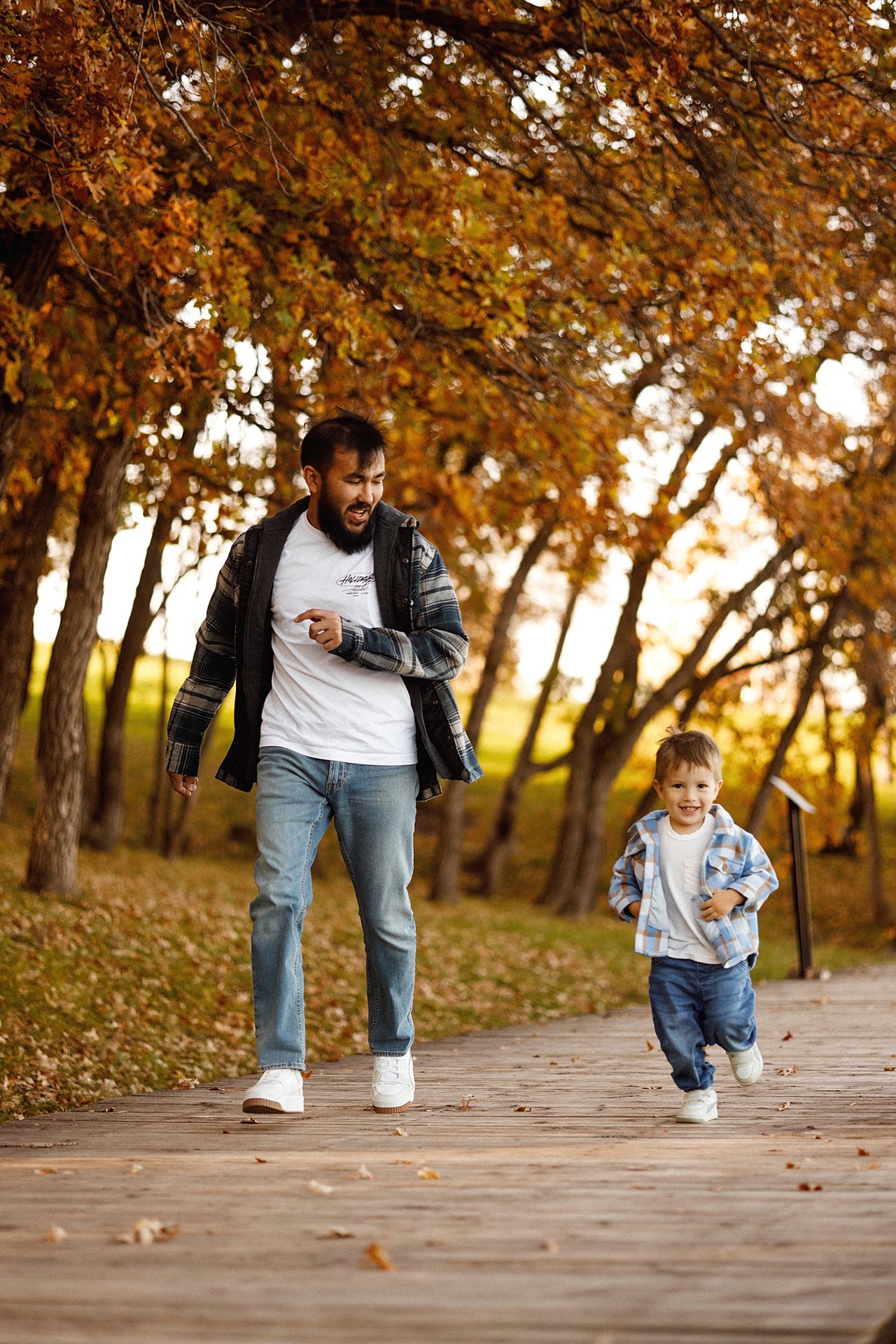 Alina and Nurali walking hand in hand with their son David along an autumn path.