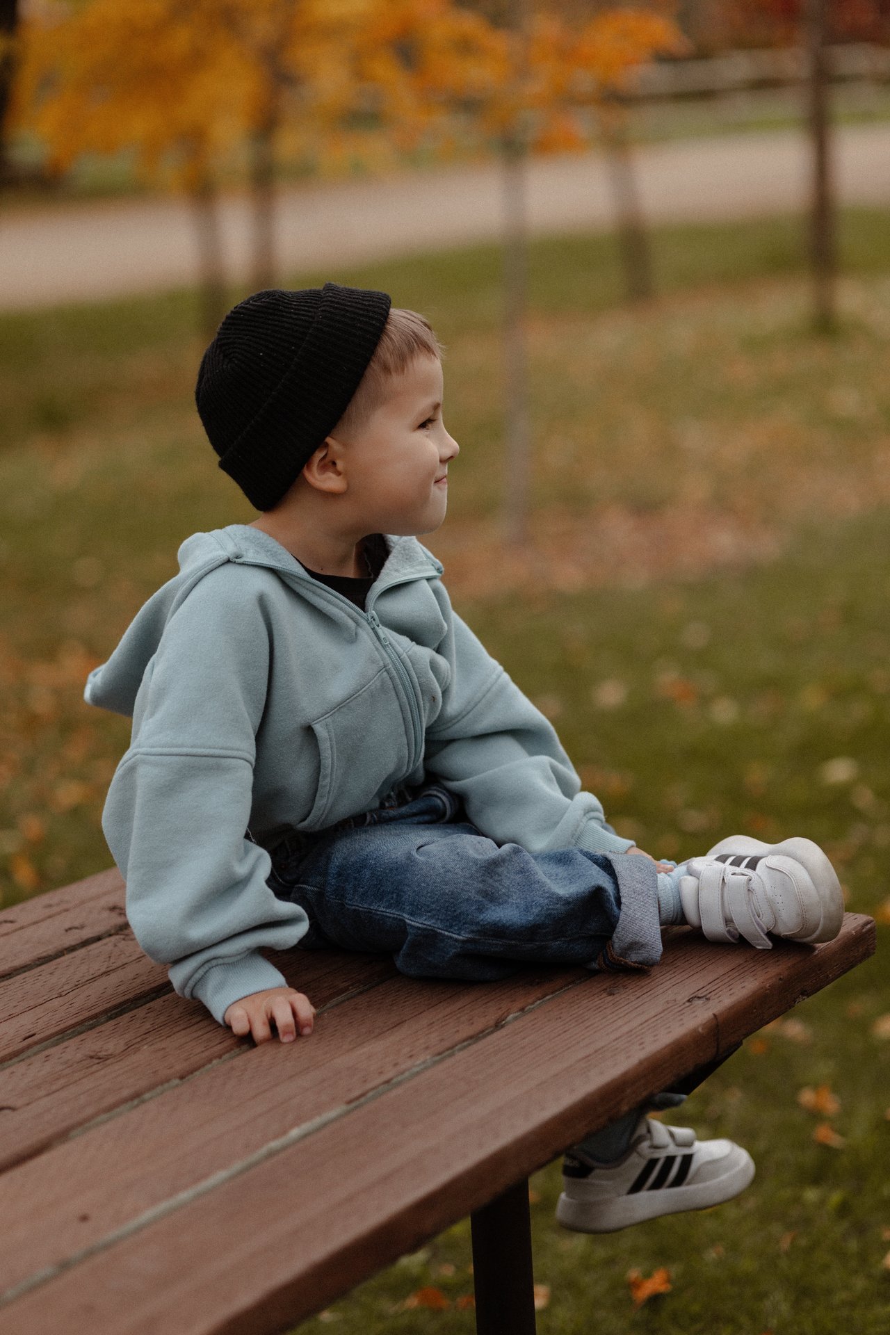 David sitting on a wooden bench in his blue jacket and black hat.