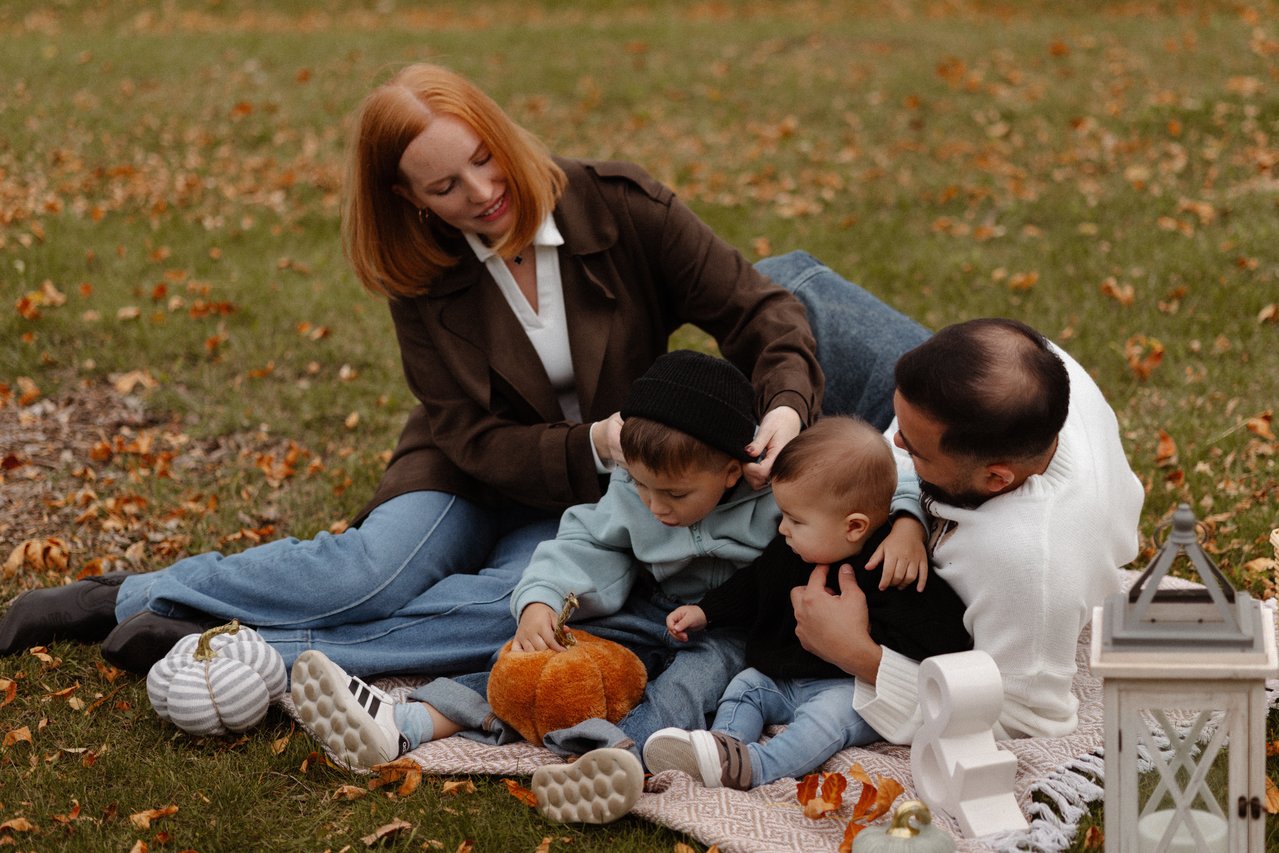Alina, Nurali and their children sitting together on a blanket outdoors.