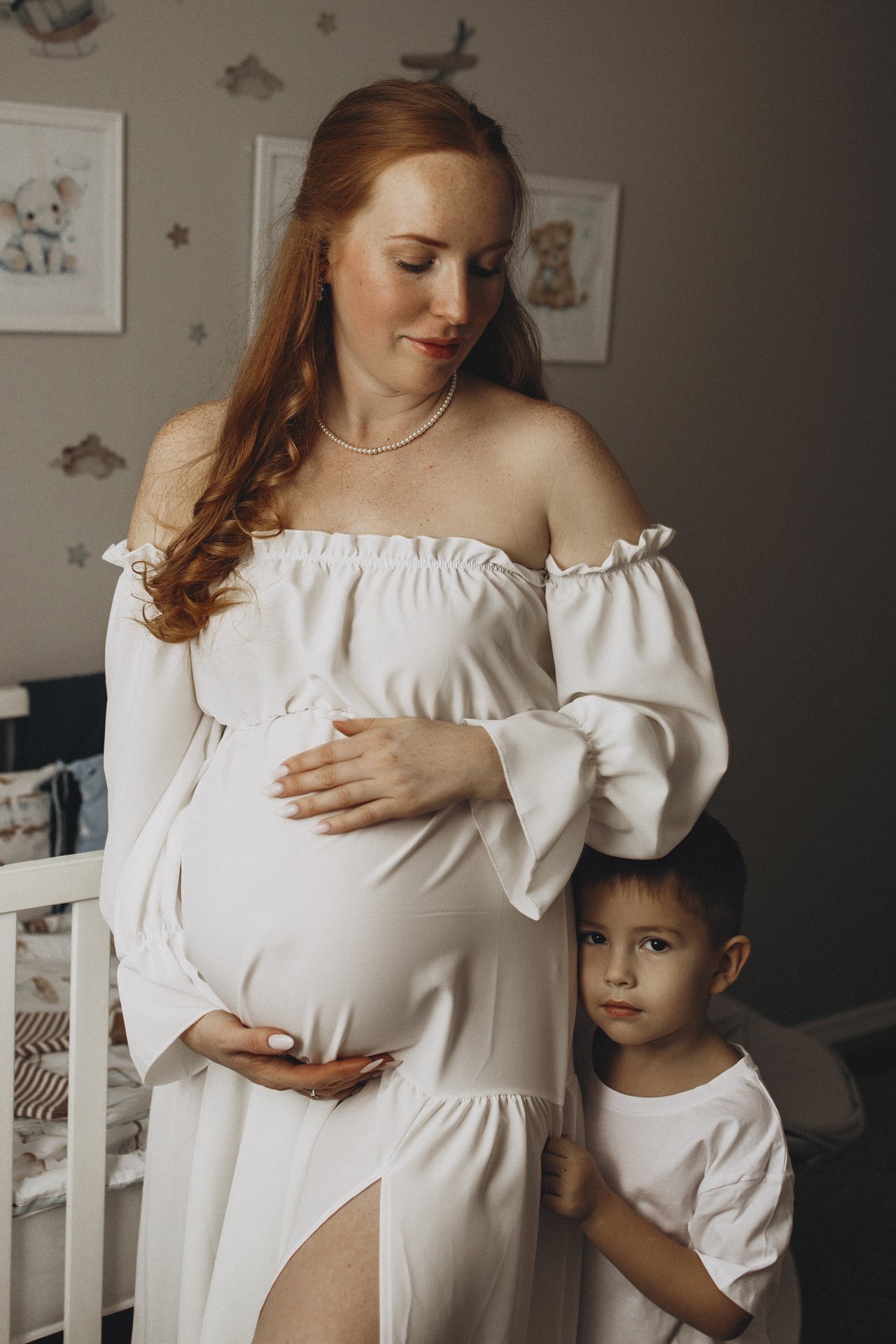 Alina resting her hands on her bump, with David standing close beside her in the nursery.