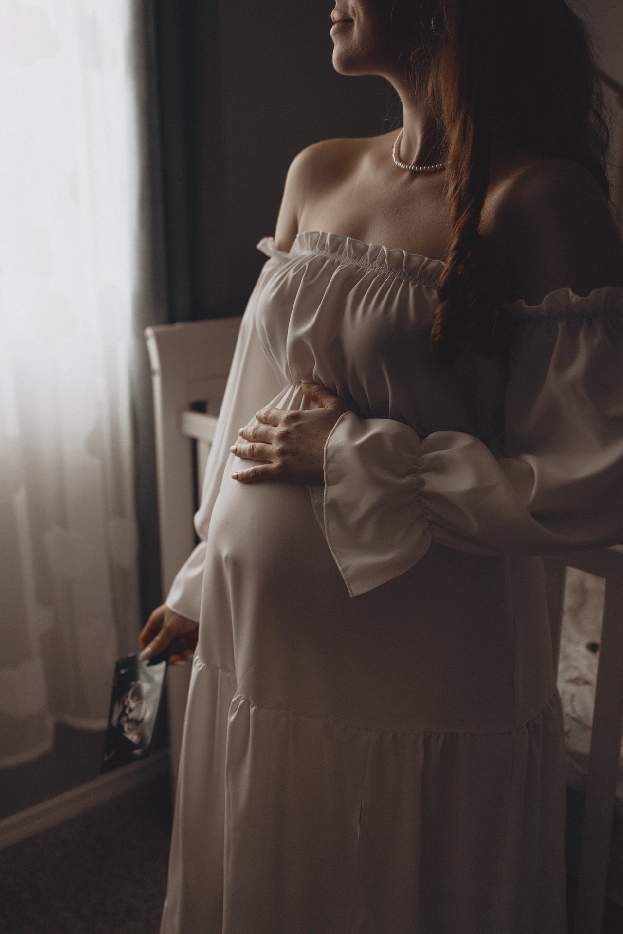 Alina standing beside the nursery window with her hands resting on her bump.