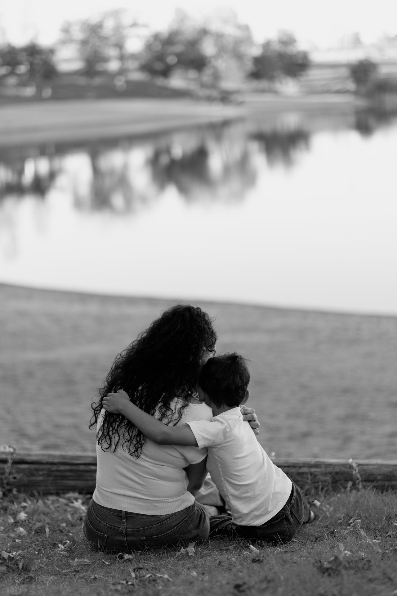 Black and white view from behind of a mother and child sitting together beside the water at Minnewasta.