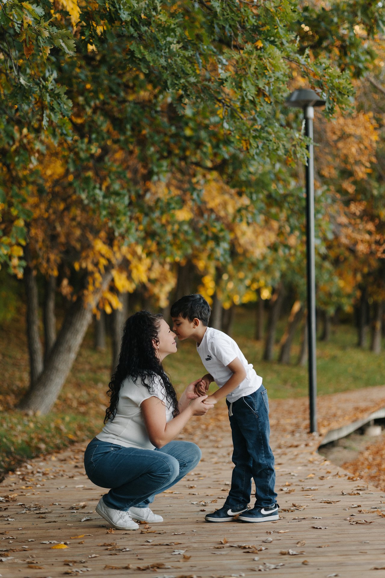 Mother crouching beside her child for a close moment on an autumn path at Minnewasta in Morden.