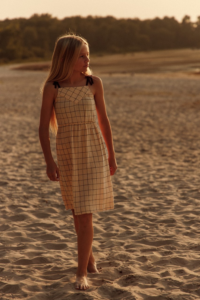 Child standing in a checked dress in warm shoreline light